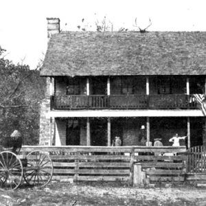 Two-story house with wooden fence and horse drawn wagon