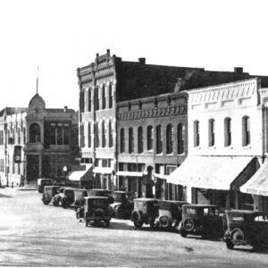 City street with buildings and cars with man crossing on foot