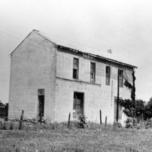 Two-story brick building with barbed wire fence and trees