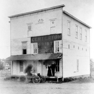 Three-story building labeled "Centerton Grist & Feed Mill" with two people and wagon in front of it