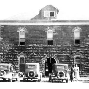 Three-story brick building with cars parked in front of it