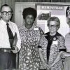 White man in glasses standing with African-American woman in a dress and two white women wearing glasses