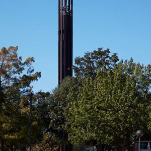 Round bell tower on college campus with trees and walking paths with benches and buildings under it