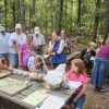 White man teaching a group of white men women and children at outdoor table with animal bones on it