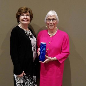 Older white woman in black coat standing next to old white woman in pink holding a blue object