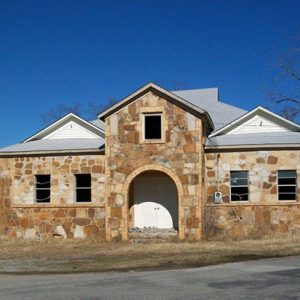 Abandoned stone-fronted building with Dutch gable roof and arched entrance way on street