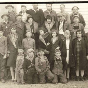 Group of young white men women and children posing with trophy outside building with wood siding