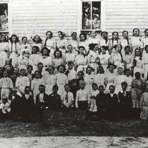 Large group of people standing before wooden building