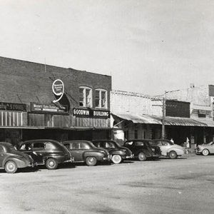 Multistory brick buildings on town street with cars parked in front of them