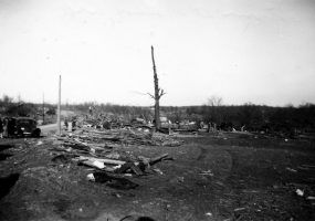 People and car parked in debris covered field with bald trees