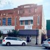 Two-story brick storefronts on street with parked white van and street lamp