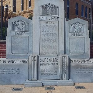 War memorial monuments and brick wall in court yard with multistory brick building behind it