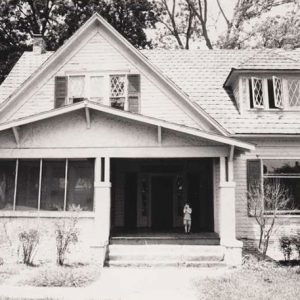 Two-story house with covered porch with child standing on porch