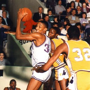 African-American men in uniform playing basketball on court with  crowd watching