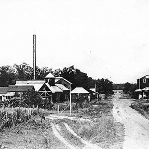 Industrial buildings on dirt road with water tower and smoke stacks