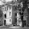 Multistory striped brick building with arched and rectangular entrances rectangular windows downspout and large trees