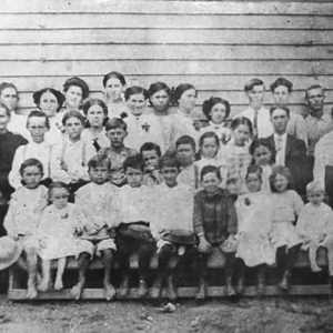 Group of white children and teachers standing outside building with wood siding