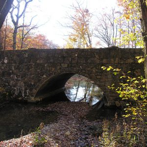 Side view of stone arch bridge over river under autumn trees