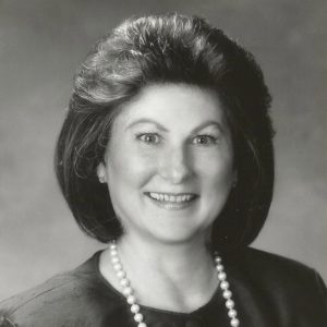 White woman smiling in dress and pearl necklace