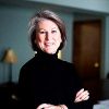 White woman smiling in black turtleneck sweater with arms crossed