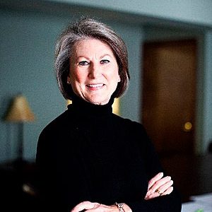 White woman smiling in black turtleneck sweater with arms crossed