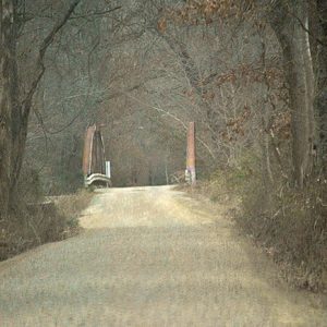 Looking down dirt road across steel arch bridge over river