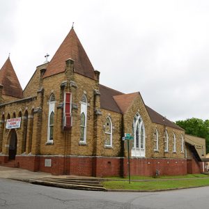 Brick church building with twin front towers and stained glass windows on street corner