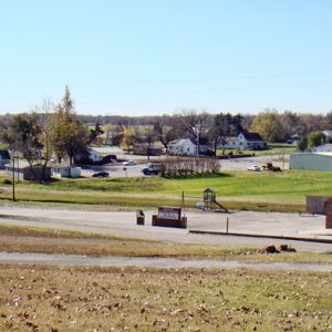 Single-story brick church building with steeple houses and town buildings on paved roads as seen from hill top