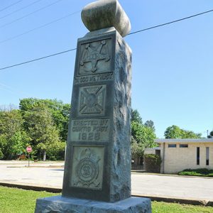 Stone monument with engraved text and shields on pedestal