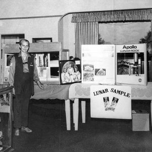 Old white woman standing in room with Apollo exhibit on table