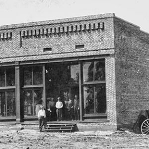 Brick storefront with large windows on dirt road