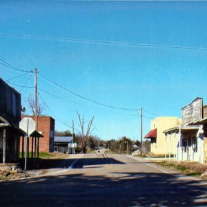 Street with storefront buildings on either side and power lines and blue sky