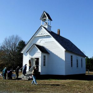 White men and women outside single-story church building with bell tower