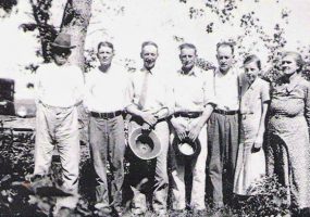 Group of white men and a woman and a girl standing together under a tree