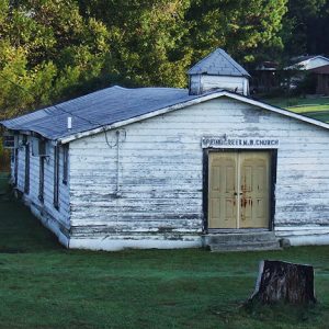 Single-story building with chipped white paint and cupola and double doors on grass