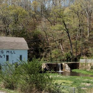 Barn with "Spring Mill 1867" written on its side and stone wall on creek with water flowing over it