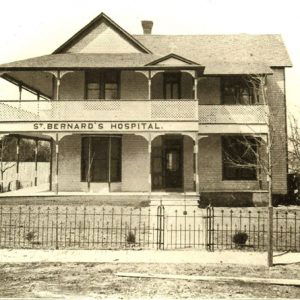 Two story brick building with ninety degree porch lattice railing and sign "Saint Bernard's Hospital"