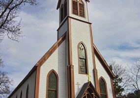 white building with darker wood trim with tall steeple tower and cross on top