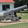 Cannon on round pedestal on concrete platform with single-story white building behind it