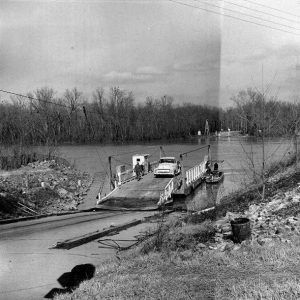 Man and truck on ferry boat on river shore