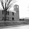 Two-story brick building with clock tower and trees