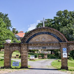 Brick arch over driveway with cross on top and "St. Joseph's Home" written on center portion