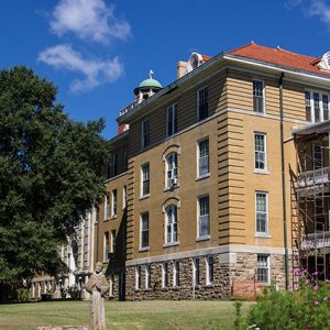 Four-story building with cupola and scaffolding on the side with a statue of man in robes in front