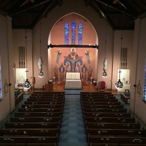 Interior of church sanctuary with rows of pews and painting of a crucified Jesus and angels behind the altar