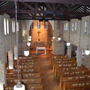 Interior of brick church sanctuary with wooden pews looking towards the altar from above