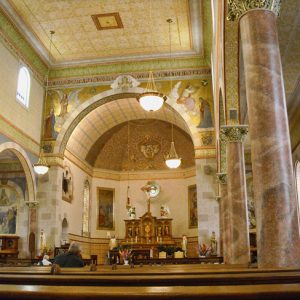 Wooden pews and altar inside multistory sanctuary room with stone columns and painted walls