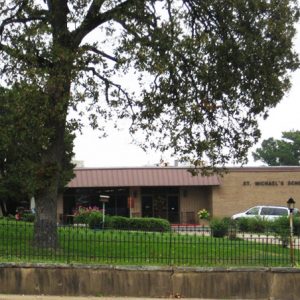 Trees inside iron fence in front of single-story brick building