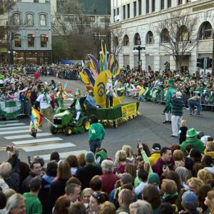 White man on tractor pulling a parade float on city street with crowd of people on both sides