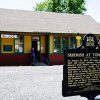 Red yellow and green building with "Skirmish at Tomahawk" historical marker sign in front of it