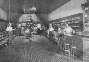Four men in dark pants, white shirts, and suspenders in drug store